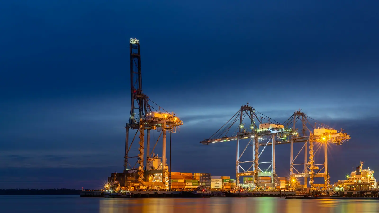 Ship-to-shore cranes lit at a container terminal at dusk